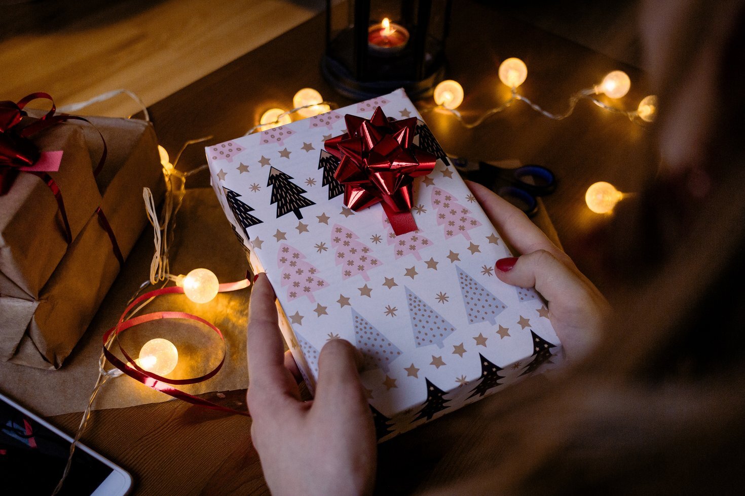 Person holding gift box with red ribbon beside string lights 1687049